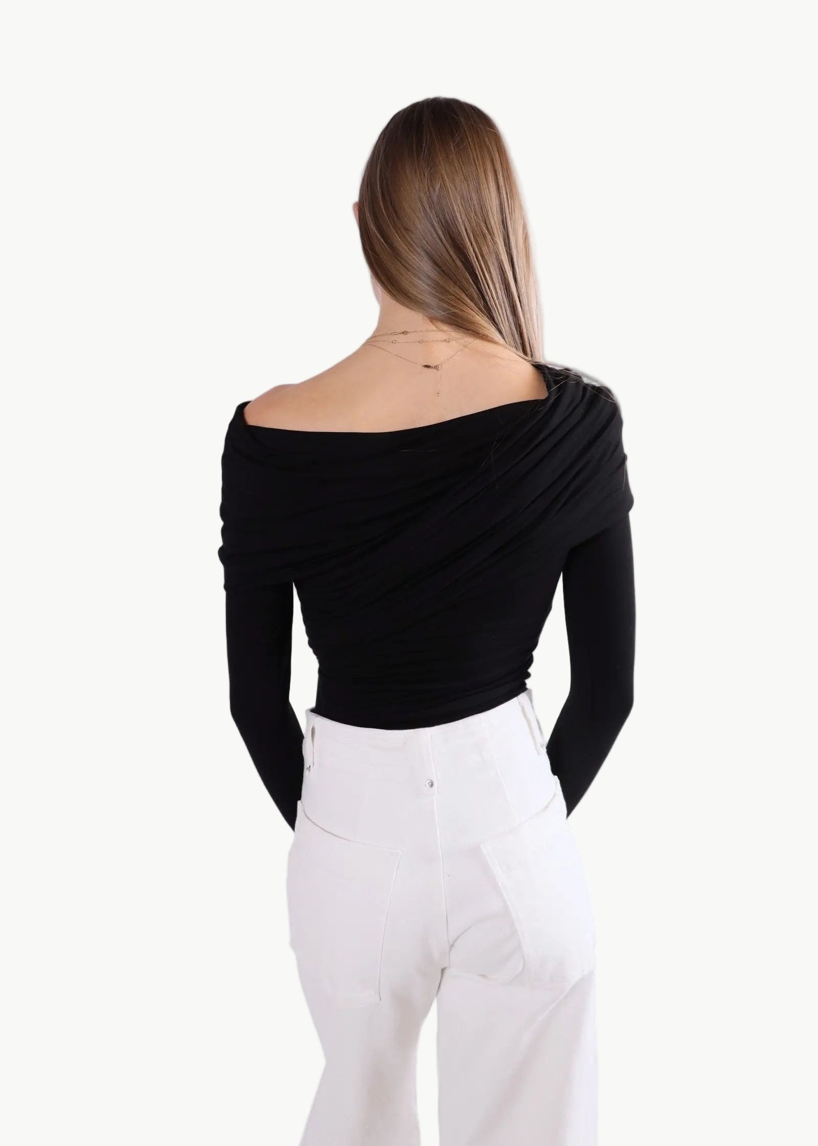 La Libéré model  wearing a black off-shoulder top and white pants on a white background