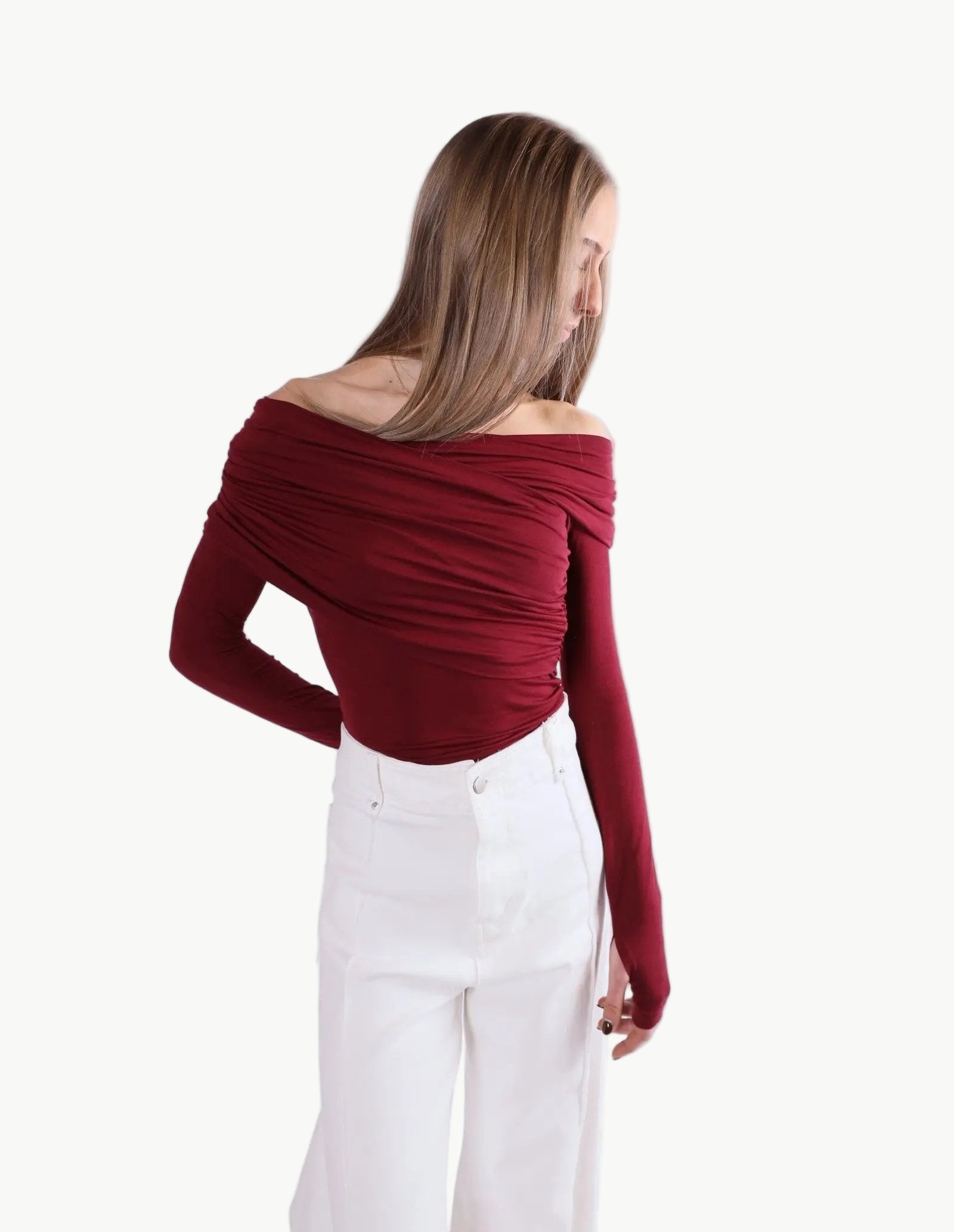 La Libéré model  wearing a burgundy off-shoulder top and white pants on a white background