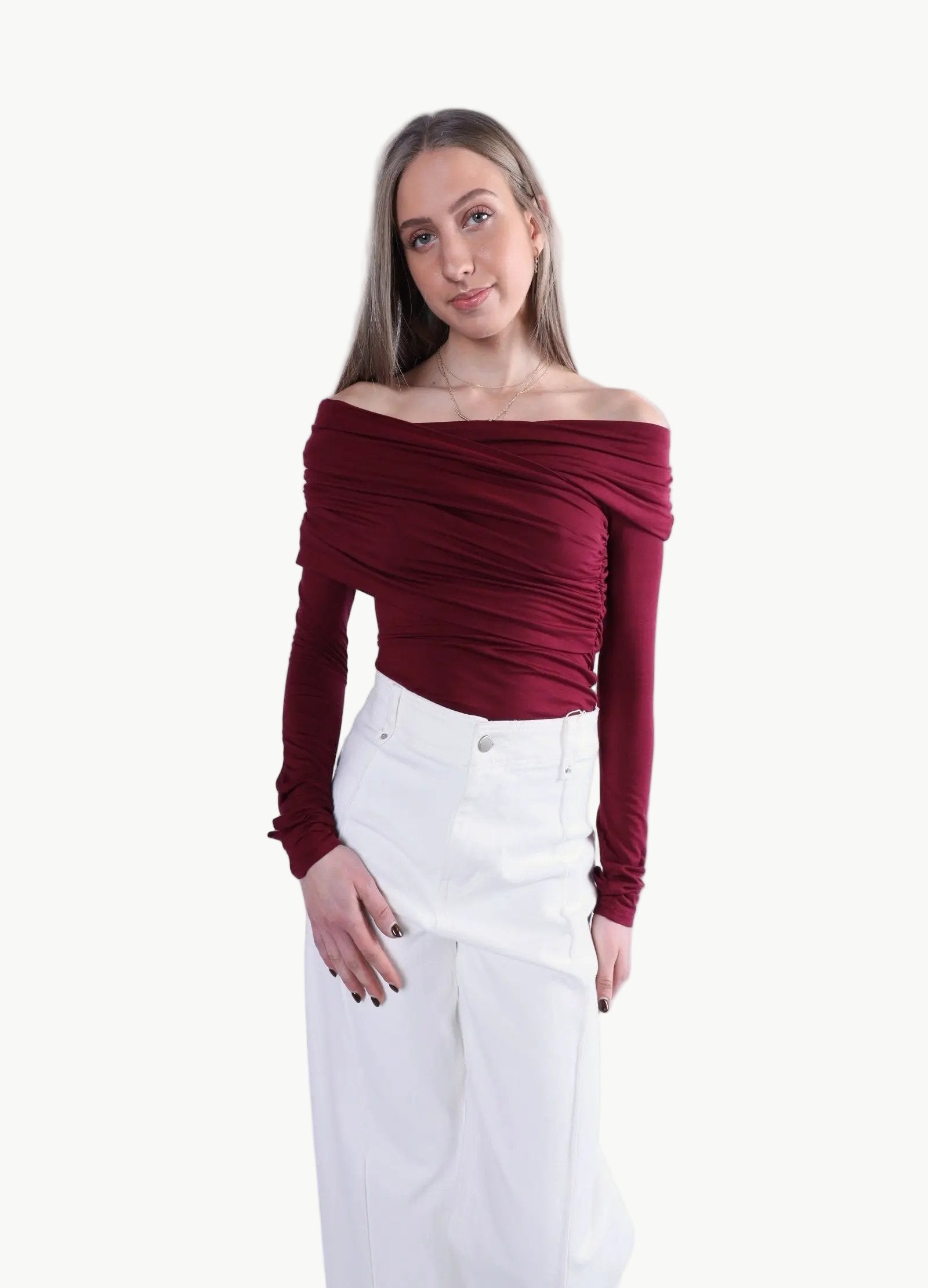 La Libéré model  wearing a burgundy off-shoulder top and white pants on a light grey background