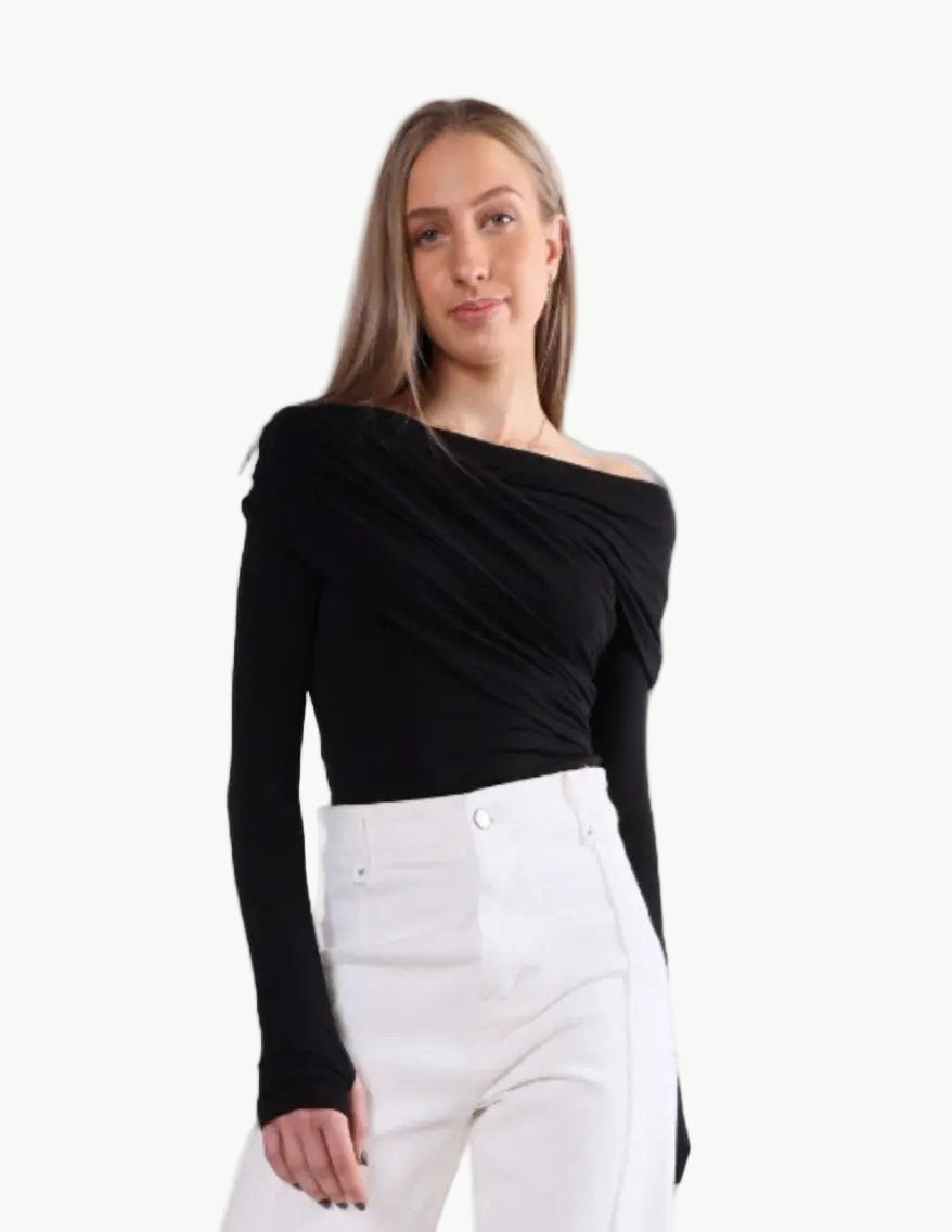 La Libéré Woman wearing a black off-shoulder top and white pants on a light grey background